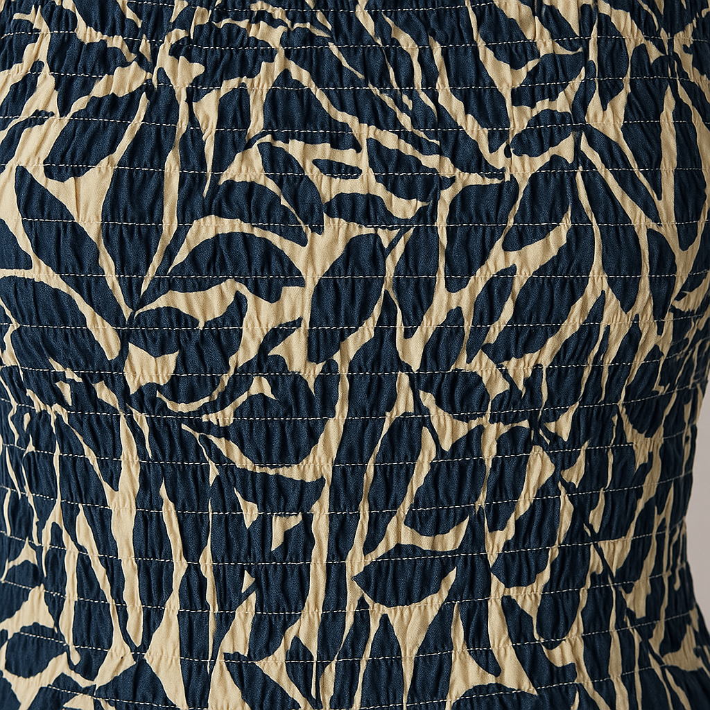 Smocked sleeveless top with blue leaf print on a cream base, featuring a fitted silhouette and round neckline.