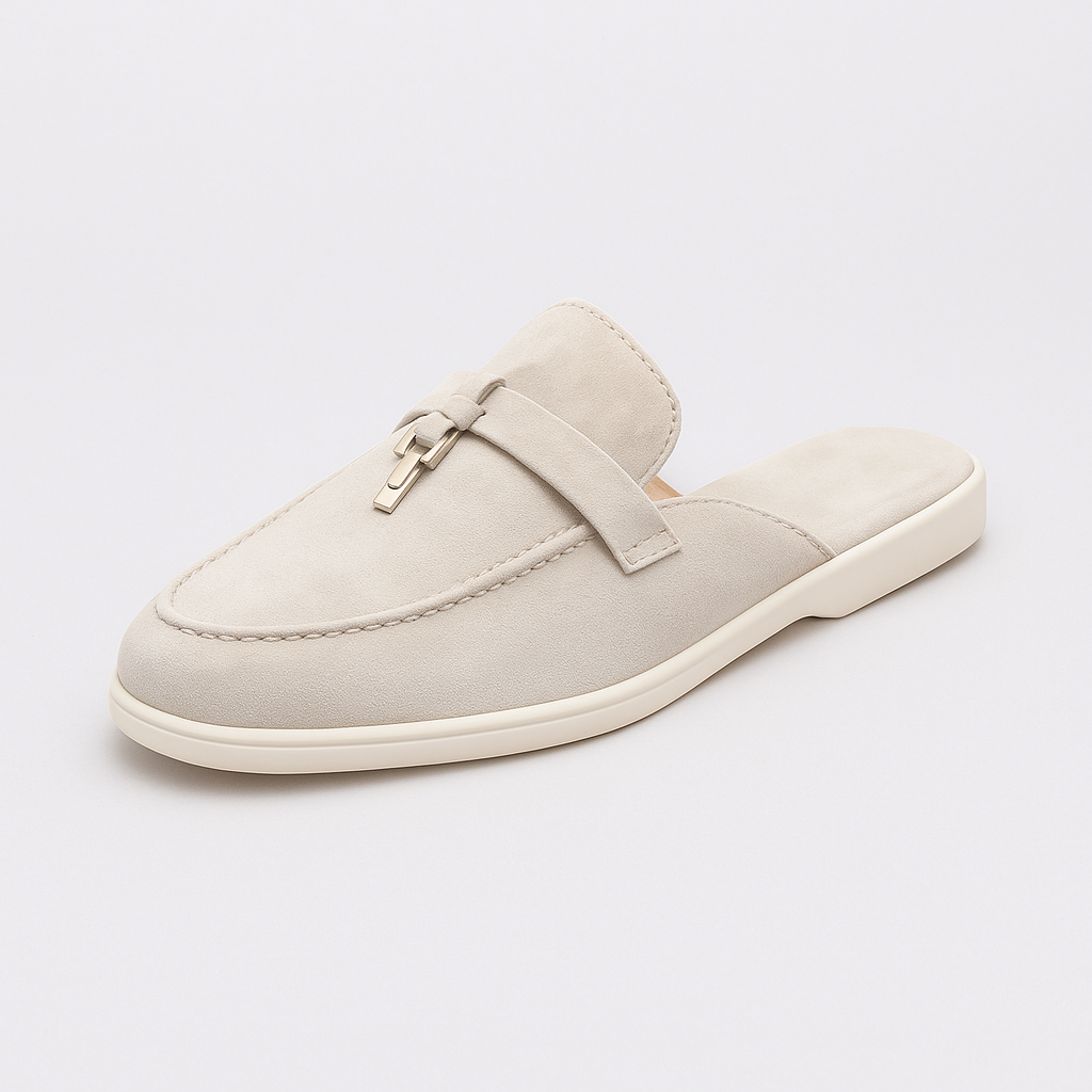 Suede mule loafer with a rounded toe, decorative strap, metal accent, and flat sole.
