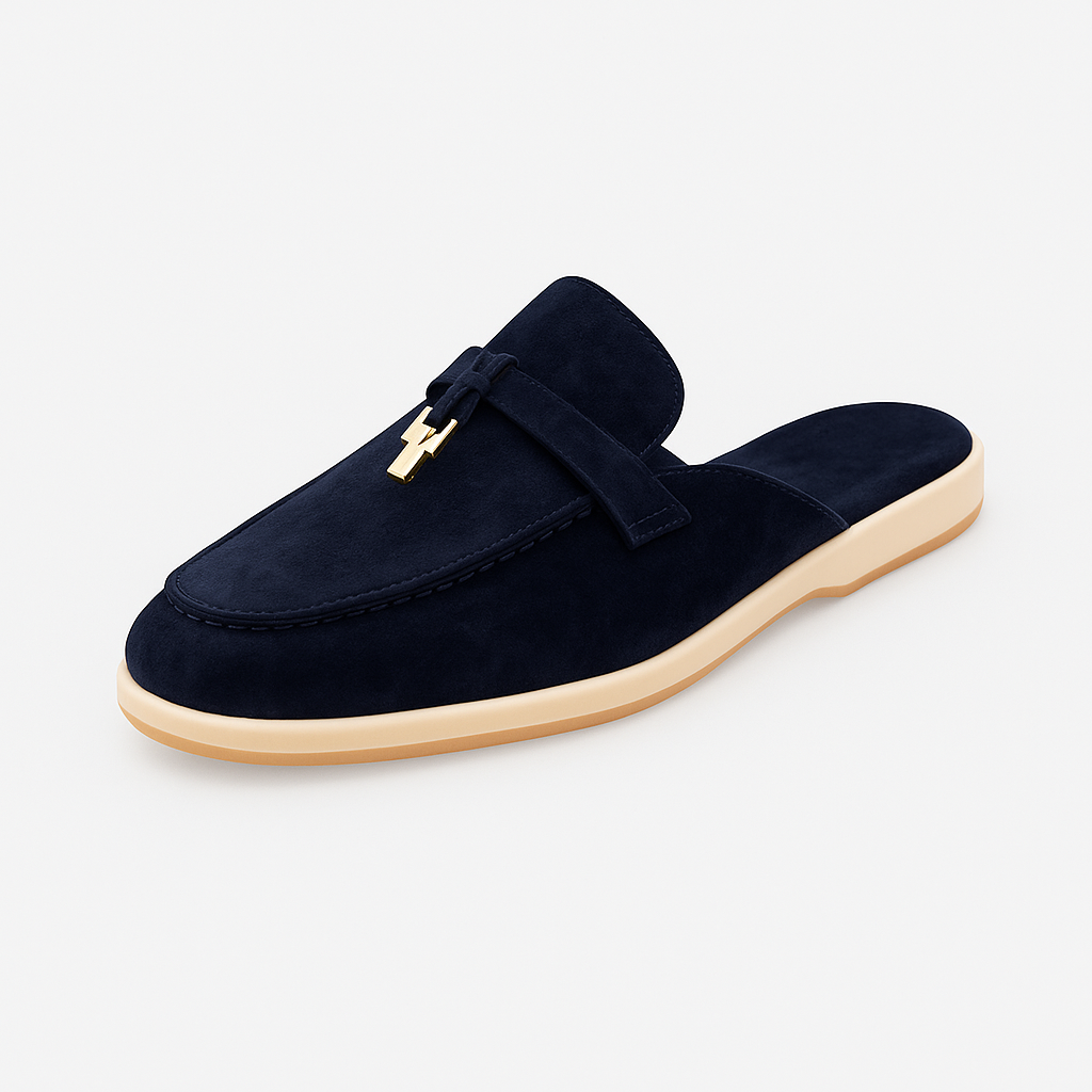 Suede mule loafer with a rounded toe, decorative strap, metal accent, and flat sole.