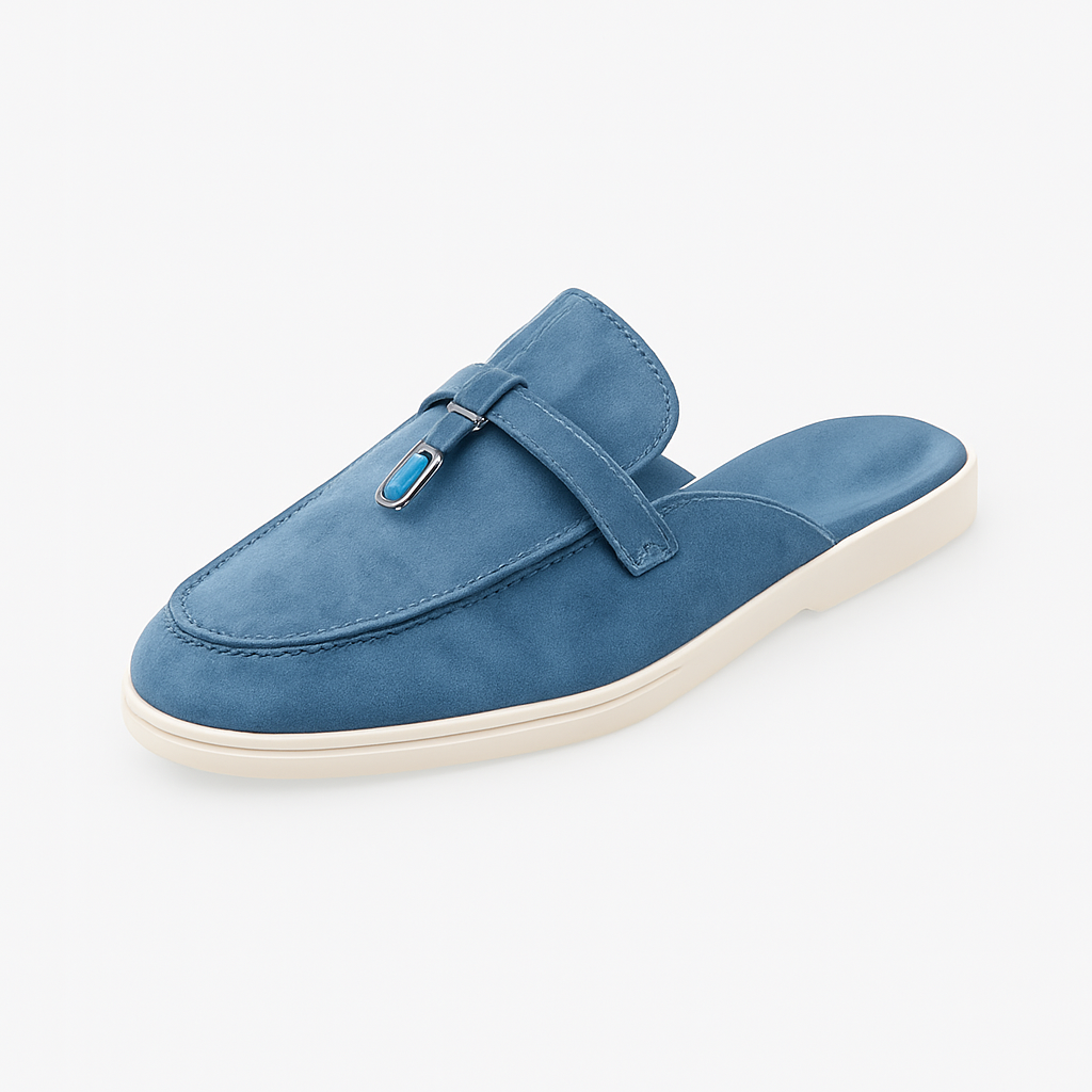 Suede mule loafer with a rounded toe, decorative strap, metal accent, and flat sole.