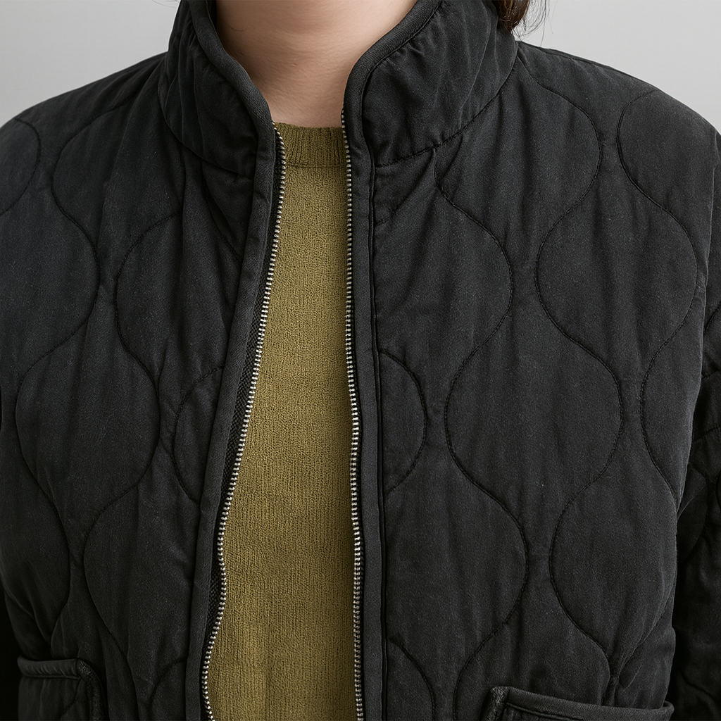 A quilted jacket featuring a high collar, full front zipper, and relaxed fit. Designed with wave-pattern stitching, two large front patch pockets, and adjustable drawstrings at the hem for a customizable fit. A minimalist yet functional outerwear piece perfect for layering in cooler weather.