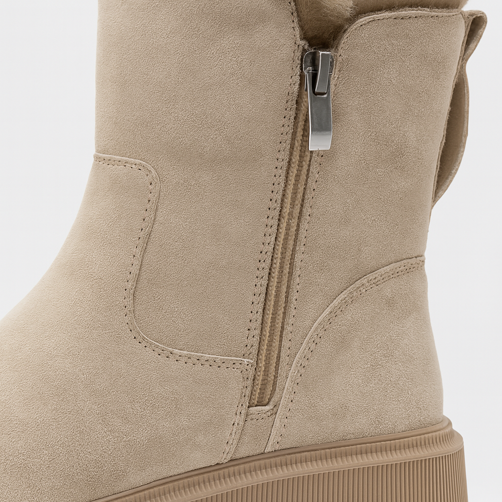 A mid-calf winter boot with a soft suede exterior, side zipper closure, pull tab at the heel, faux-fur lining, and a chunky ridged sole.