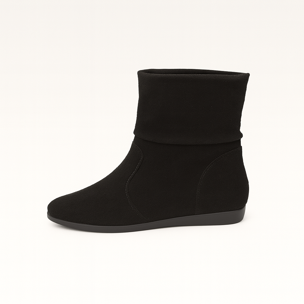 A pair of suede ankle boots with a slouchy, relaxed fit and flat soles. The boots feature a minimalist design with subtle stitching details and are shown worn on a model’s feet against a neutral background.