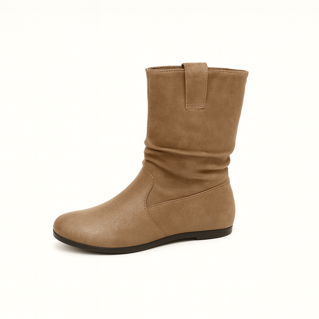 A pair of suede ankle boots with a slouchy, relaxed fit and flat soles. The boots feature a minimalist design with subtle stitching details and are shown worn on a model’s feet against a neutral background.